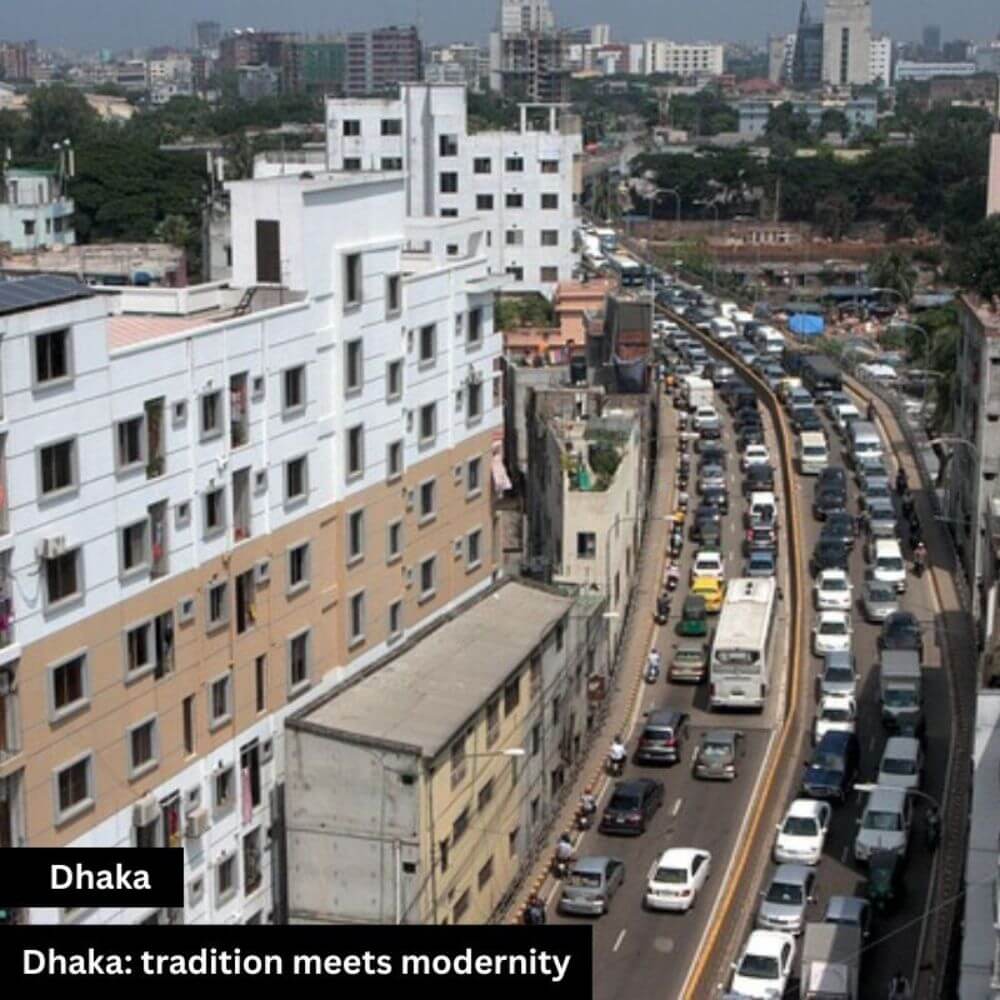 A bustling street view of Dhaka, the capital of Bangladesh, where cars and vehicles move along both sides of the road. Tall building walls line the street, reflecting the city’s urban atmosphere. The scene captures Dhaka’s fast-paced life and metropolitan energy